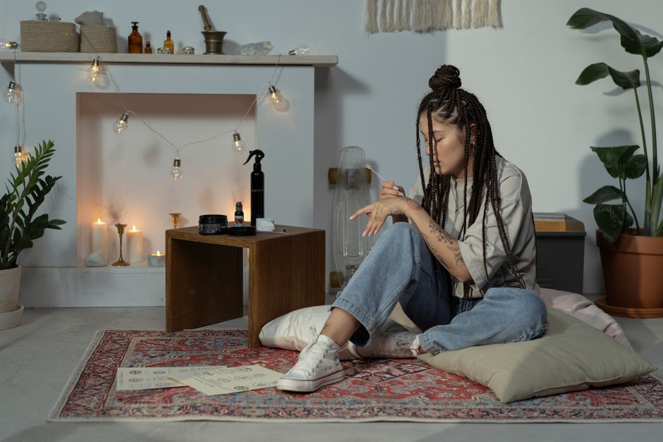 Woman with Afro braids in a cozy boho room. Featuring candles, plants, and cushions.